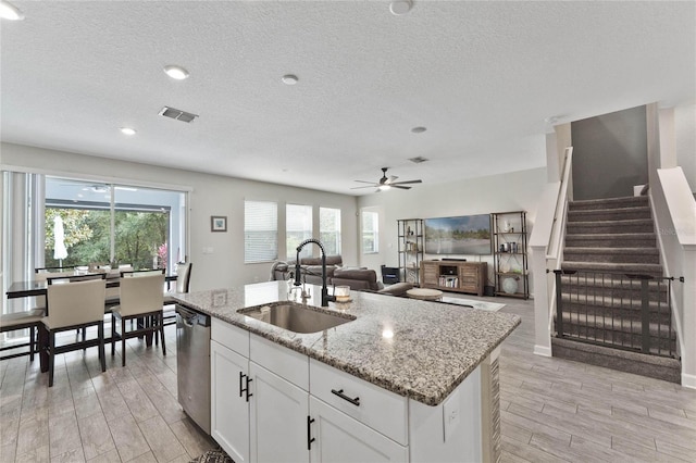 kitchen with light stone countertops, visible vents, a sink, dishwasher, and light wood-type flooring