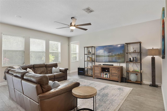 living area with visible vents, baseboards, light wood-style floors, and a ceiling fan