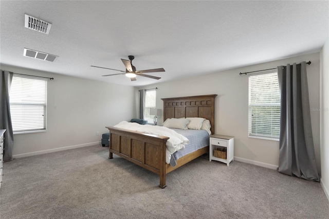 carpeted bedroom with a textured ceiling, baseboards, visible vents, and ceiling fan