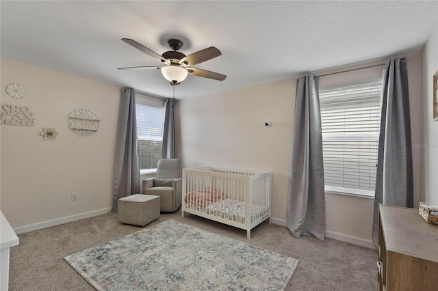 bedroom with a ceiling fan, baseboards, a crib, a textured ceiling, and light colored carpet