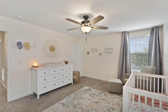 carpeted bedroom featuring a nursery area, a ceiling fan, and baseboards