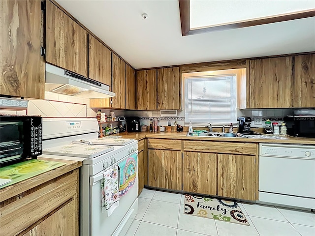 kitchen featuring tasteful backsplash, under cabinet range hood, light tile patterned floors, white appliances, and a sink