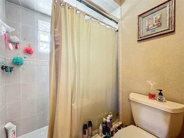 full bathroom featuring a tile shower, toilet, and a textured wall