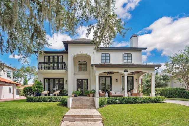 mediterranean / spanish-style house with stucco siding, french doors, a front yard, a balcony, and a chimney