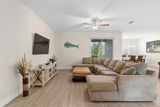 living room with visible vents, light wood-style flooring, ceiling fan with notable chandelier, and baseboards