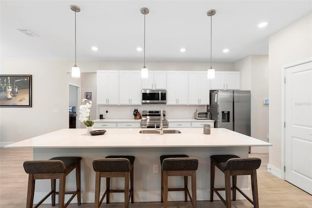 kitchen featuring appliances with stainless steel finishes, white cabinetry, a kitchen bar, and a sink