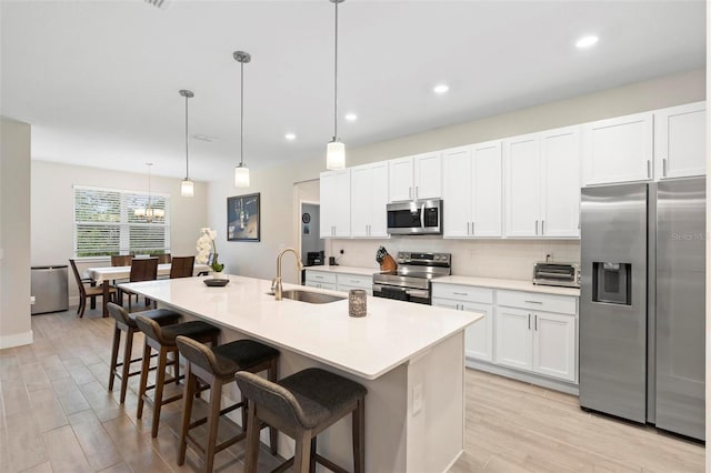 kitchen with a kitchen island with sink, a sink, backsplash, appliances with stainless steel finishes, and a breakfast bar area