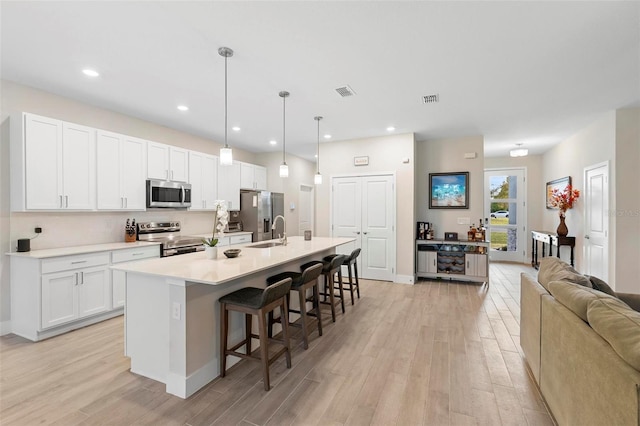 kitchen with a kitchen bar, an island with sink, appliances with stainless steel finishes, light wood-style floors, and white cabinets