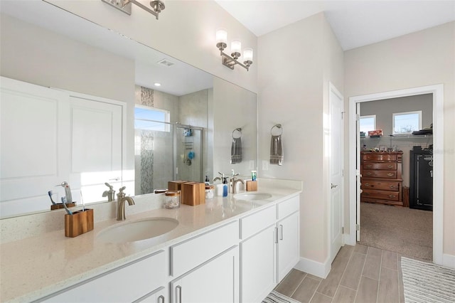 full bathroom featuring double vanity, a stall shower, a walk in closet, and a sink