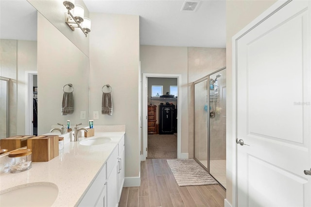 full bath with wood finish floors, visible vents, a walk in closet, a sink, and a shower stall