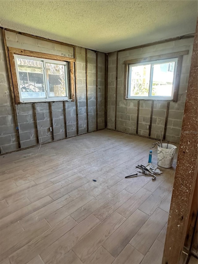 unfurnished room featuring a textured ceiling, concrete block wall, and wood finished floors