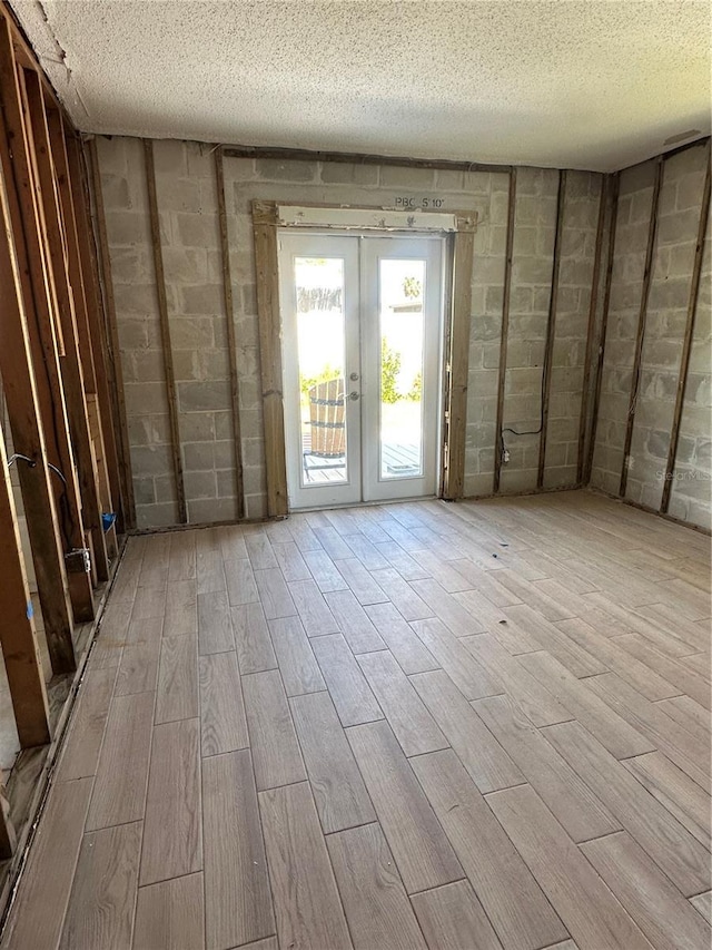 empty room featuring french doors, a textured ceiling, concrete block wall, and wood finished floors