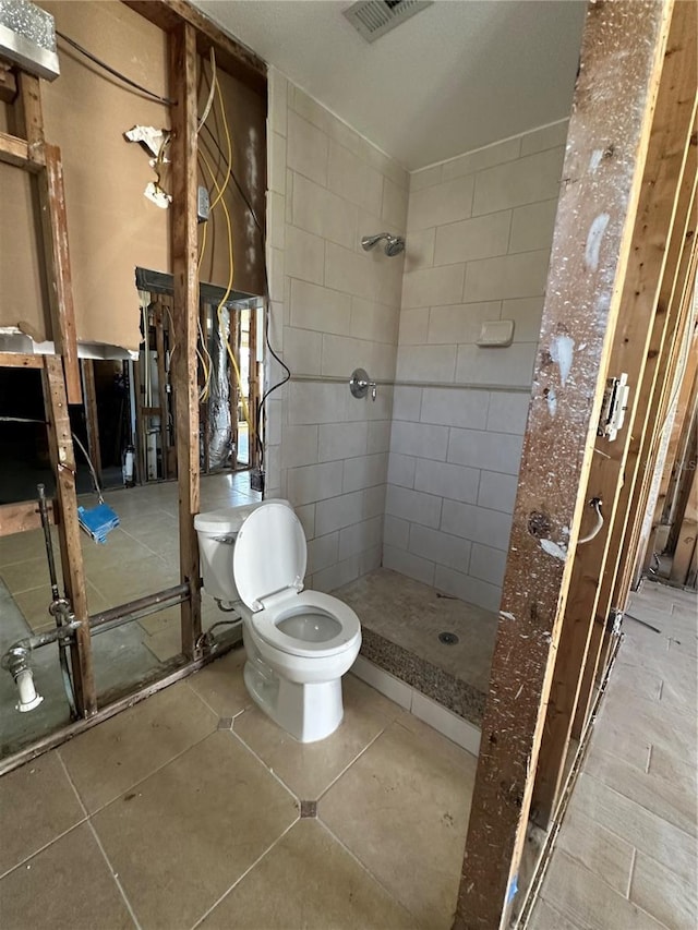 bathroom with tile patterned flooring, visible vents, toilet, and tiled shower