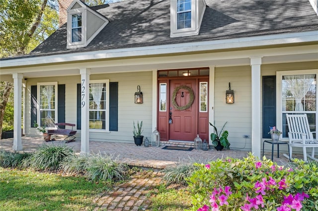 doorway to property with covered porch and a shingled roof