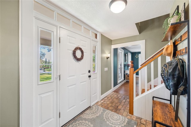 foyer featuring stairway, baseboards, and a textured ceiling