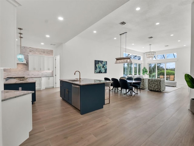 kitchen featuring a center island with sink, white cabinetry, a sink, stainless steel dishwasher, and tasteful backsplash