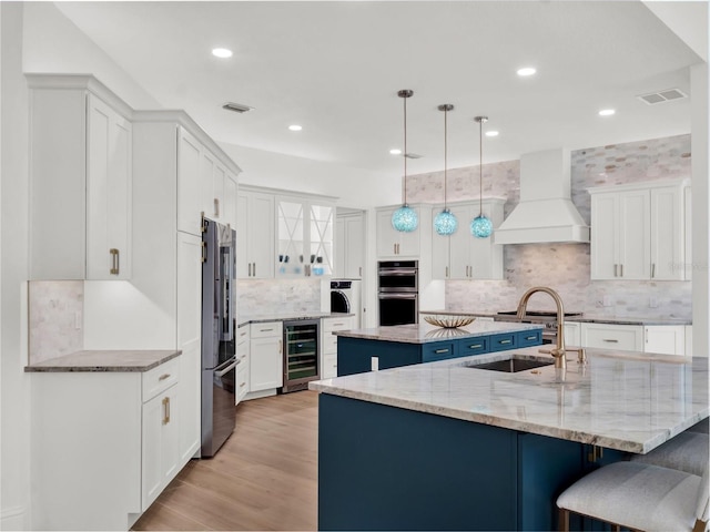 kitchen with beverage cooler, a center island with sink, premium range hood, visible vents, and high quality fridge