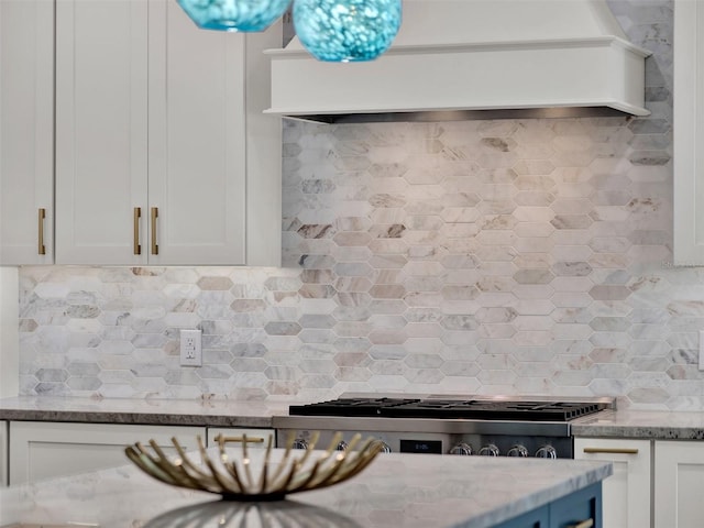 kitchen with light stone counters, backsplash, white cabinets, and premium range hood