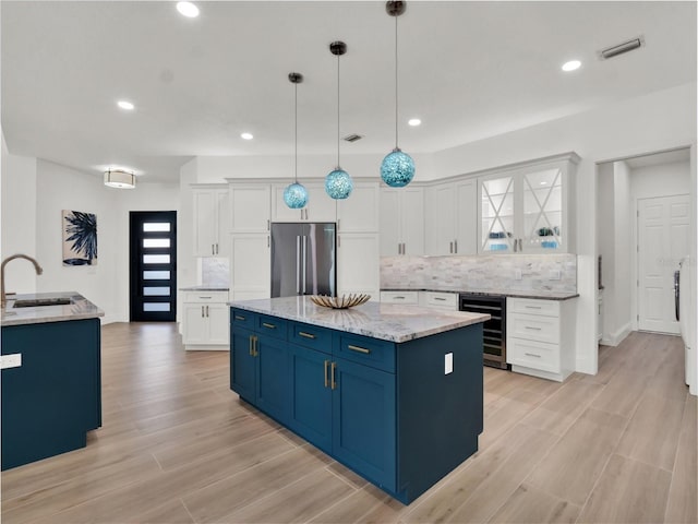 kitchen featuring beverage cooler, visible vents, blue cabinetry, a sink, and stainless steel refrigerator