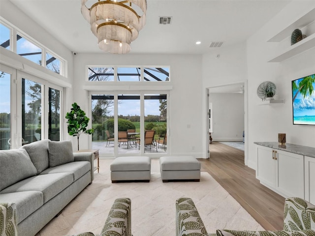 living area with visible vents, light wood-style flooring, a high ceiling, and a healthy amount of sunlight