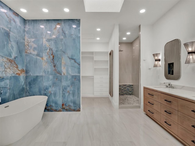 bathroom with tile walls, a freestanding bath, a skylight, tiled shower, and vanity