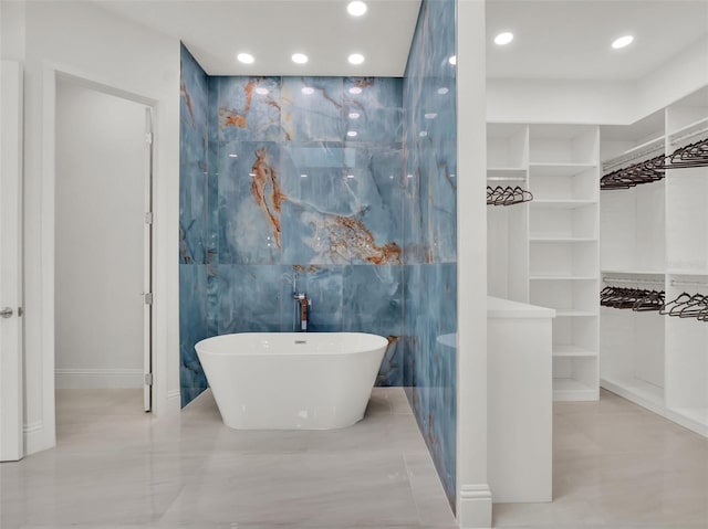 full bathroom with recessed lighting, a walk in closet, a freestanding bath, and tile walls