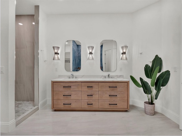 bathroom with double vanity, tiled shower, baseboards, and a sink