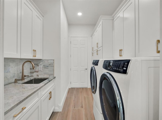 washroom featuring a sink, cabinet space, light wood finished floors, baseboards, and washing machine and clothes dryer