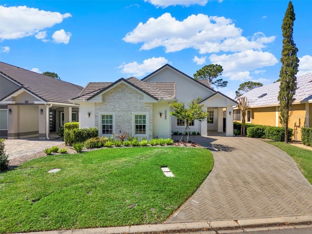 ranch-style house featuring a front yard, decorative driveway, a tile roof, and stucco siding