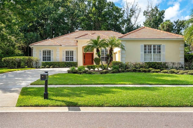 mediterranean / spanish-style house featuring a tiled roof, stucco siding, driveway, and a front yard