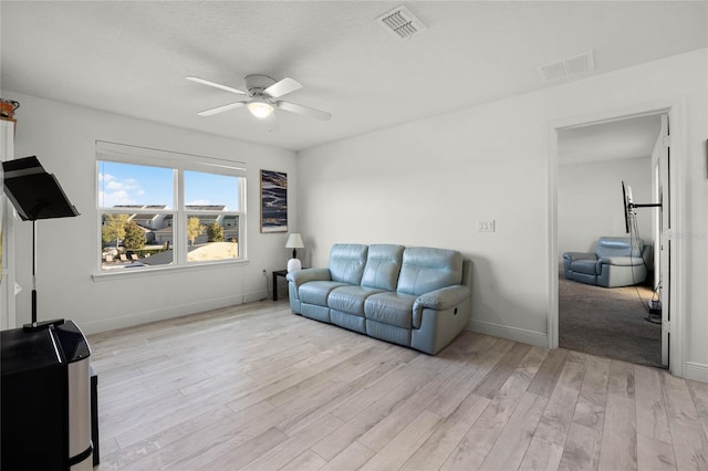 living area featuring baseboards, visible vents, light wood finished floors, and ceiling fan