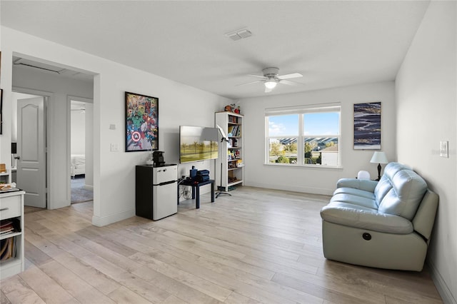 living area featuring baseboards, a ceiling fan, visible vents, and light wood-type flooring