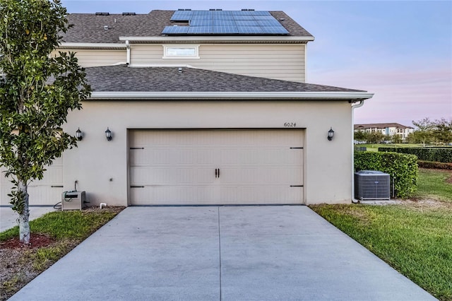 garage with roof mounted solar panels, central AC unit, and concrete driveway