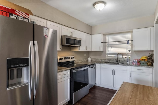 kitchen with dark wood-type flooring, dark stone countertops, appliances with stainless steel finishes, white cabinetry, and a sink