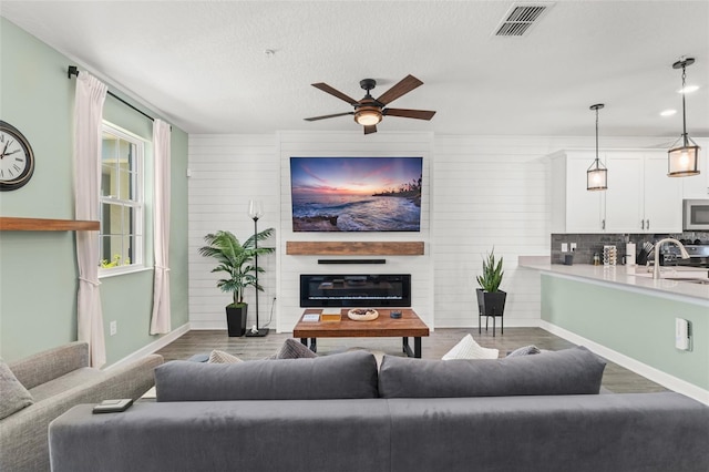 living area featuring a ceiling fan, baseboards, wood finished floors, visible vents, and a large fireplace