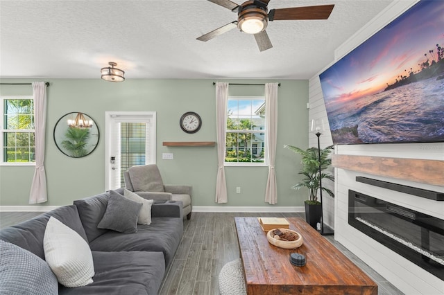 living area with a ceiling fan, wood finished floors, baseboards, a textured ceiling, and a glass covered fireplace