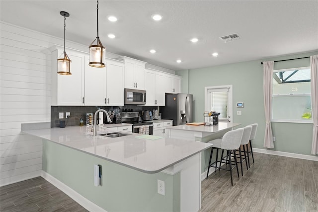 kitchen featuring wood finished floors, visible vents, a sink, decorative backsplash, and appliances with stainless steel finishes