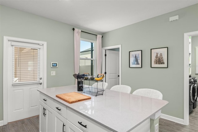 kitchen featuring white cabinetry, wood finished floors, washing machine and dryer, and light stone countertops