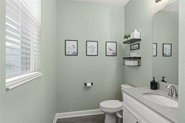 bathroom featuring baseboards, toilet, wood finished floors, and vanity