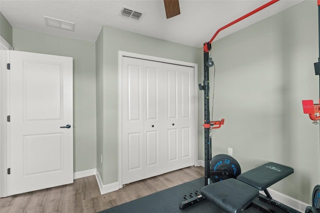 workout room with a ceiling fan, wood finished floors, visible vents, and baseboards