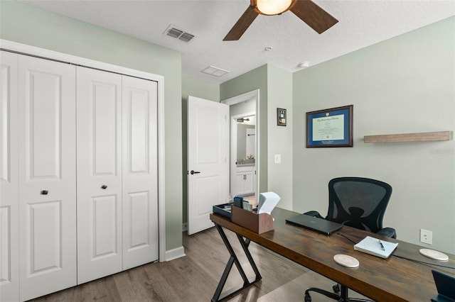 home office with visible vents, a textured ceiling, ceiling fan, and wood finished floors