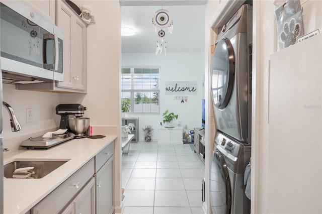 laundry area with laundry area, stacked washer / dryer, light tile patterned flooring, and a sink