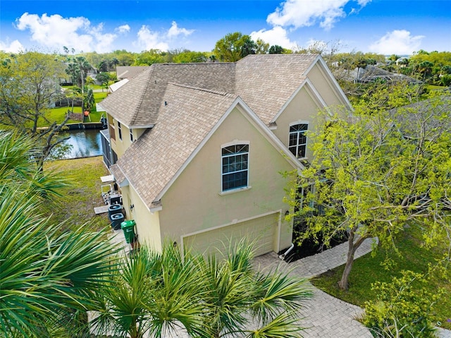 view of side of property featuring stucco siding, an attached garage, and a shingled roof