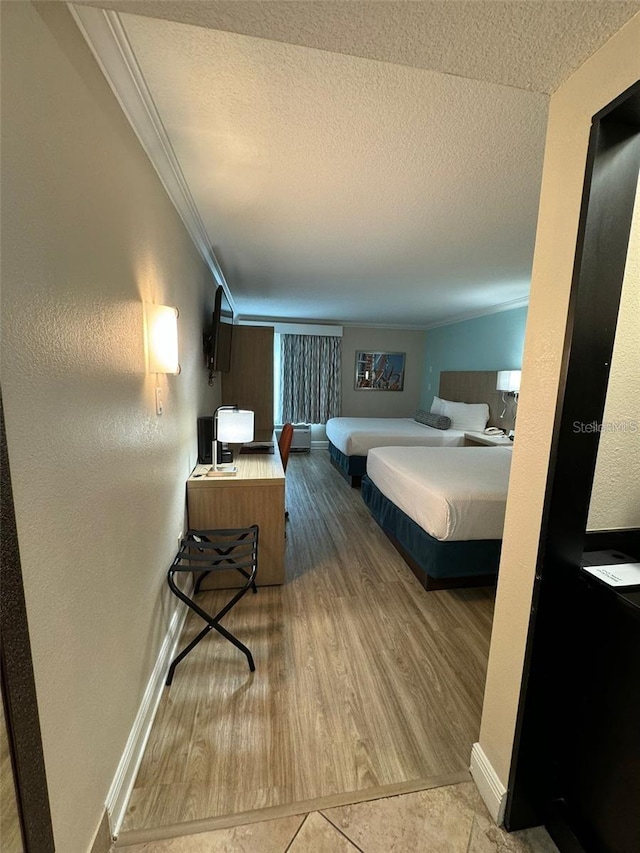 bedroom with wood finished floors, a textured ceiling, baseboards, and ornamental molding