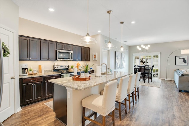 kitchen with stainless steel appliances, dark brown cabinetry, a breakfast bar area, and light wood-style flooring