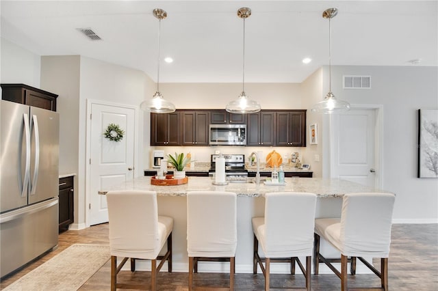 kitchen with dark brown cabinetry, visible vents, appliances with stainless steel finishes, and a kitchen bar