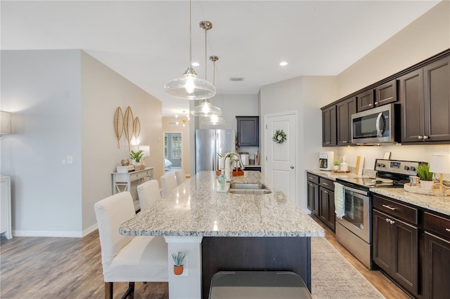 kitchen with dark brown cabinets, a breakfast bar, light stone counters, stainless steel appliances, and a sink