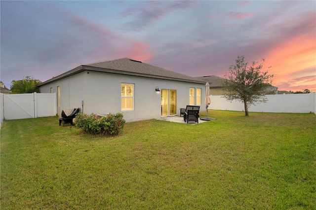 back of house with a gate, a fenced backyard, stucco siding, a patio area, and a lawn