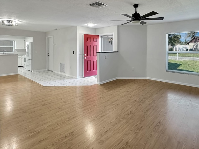 unfurnished living room with baseboards, light wood-style floors, visible vents, and a textured ceiling