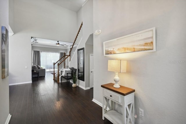 hallway with baseboards, a high ceiling, wood finished floors, and stairs